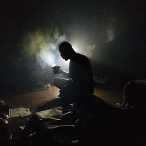 Silhouette of shamen siting crosslegged in the dark preparing a bowl of herbal medicine