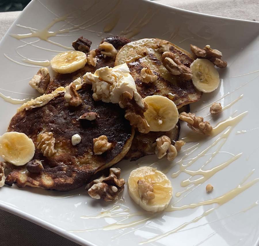 Plate of banana pancakes topped with bananas, walnuts, yogurt & honey