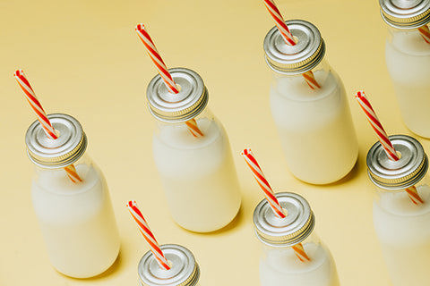 row of small milk jars with red & white straws on pastel yellow background