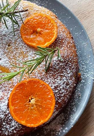 close up of clementine cake with sliced clementine, thyme and icing sugar decoration