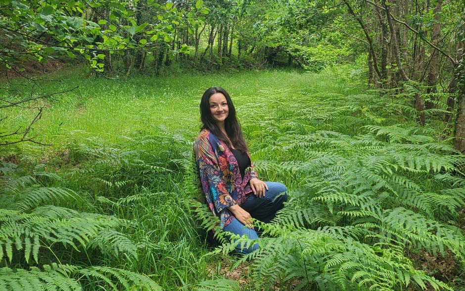 Claire kneeling in the woods, surrounded by lush green ferns